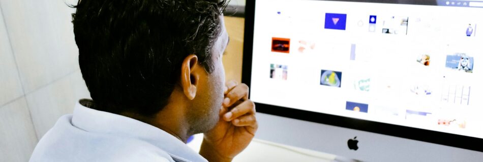 man sitting in front of silver Apple iMac on table
